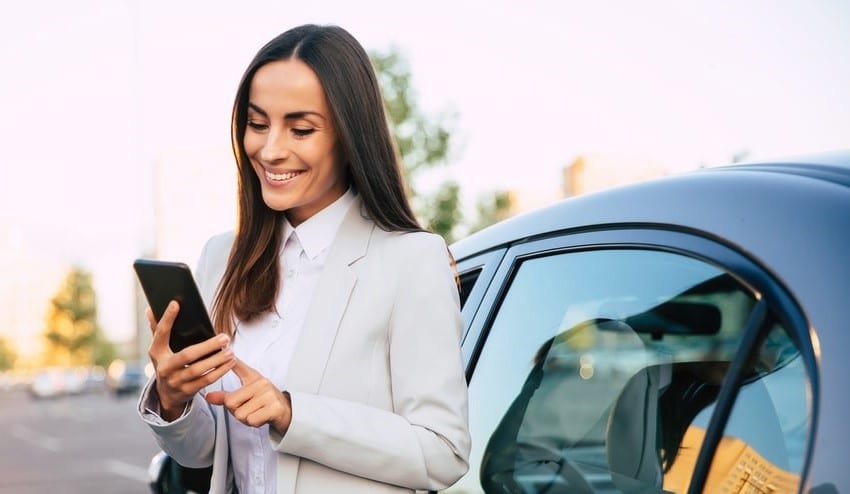 Businesswoman looking at her phone while standing outside her car.