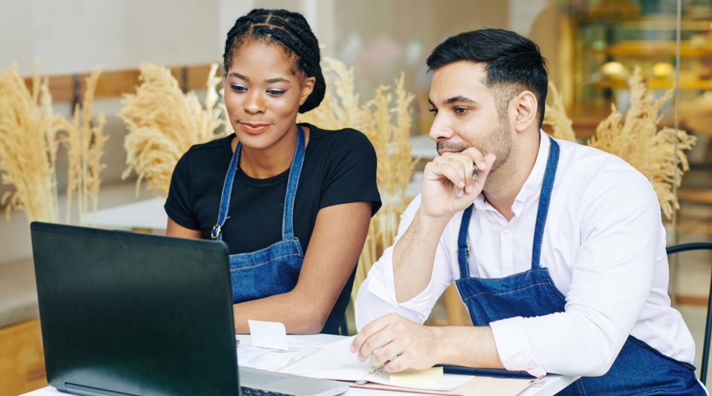 Restaurant owners in aprons looking at laptop