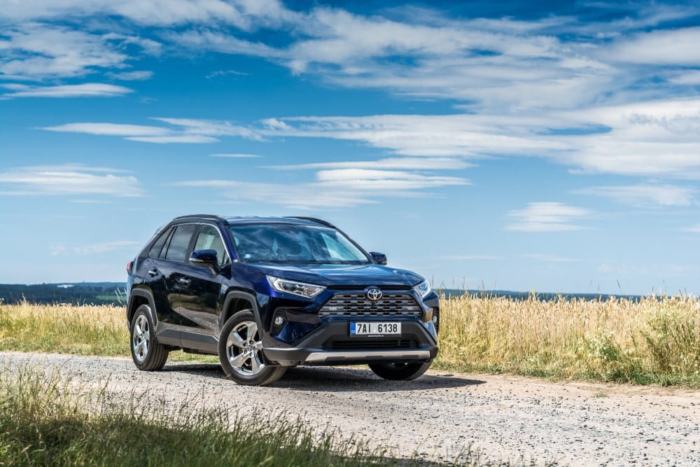 Car Insurance Banner - Black 4X4 vehicle parked on a gravel road in front of grass overlooking the ocean.