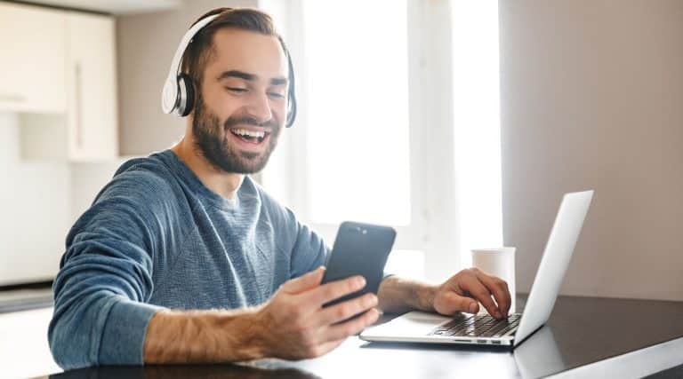 Smiling man using laptop and looking at phone