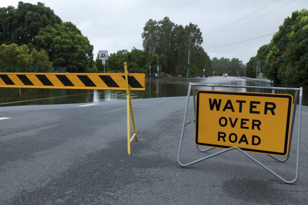 Water across road sign, in front of water covering a wide road.