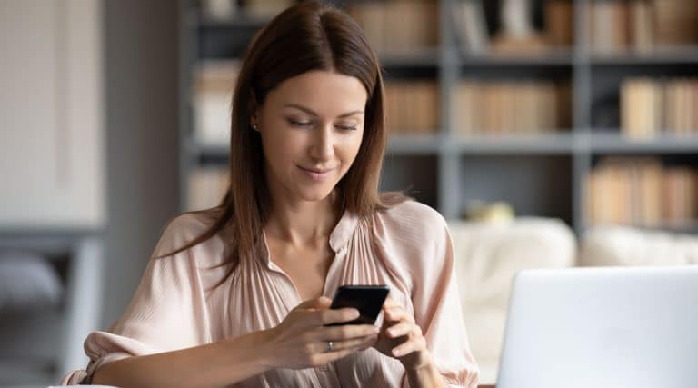 Woman looking at her phone next to her laptop