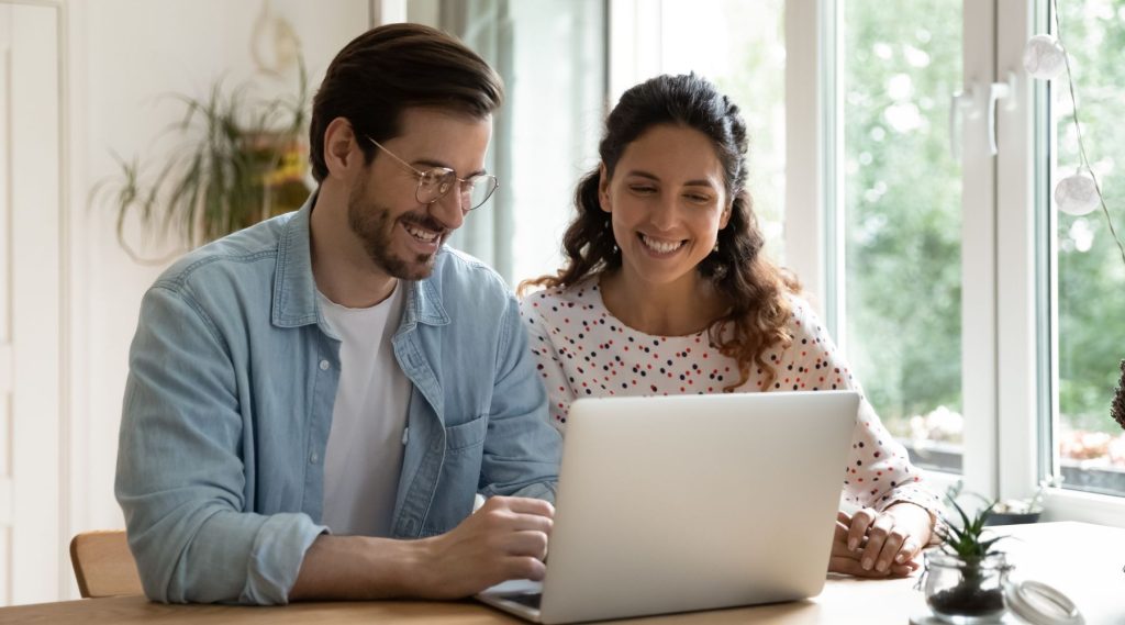 Happy couple sitting at table using laptop