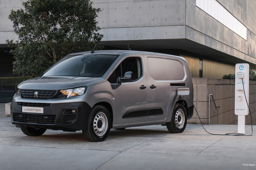 Peugeot e-partner grey van plugged into charging station.