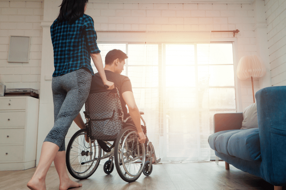 Man in a wheelchair looking out the window while being pushed by a woman